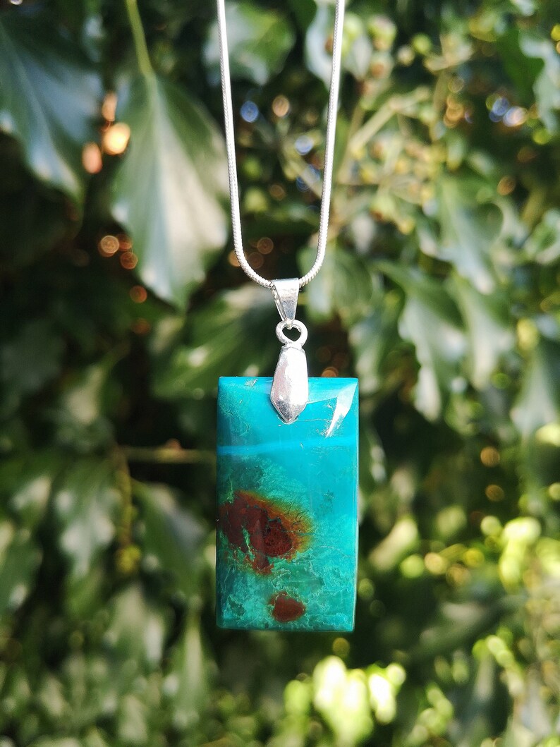 Pu&ograve; includere: Una collana con pendente rettangolare con catena d'argento. Il pendente &egrave; un vivace mix di turchese e verde acqua con inclusioni rossastre. Il pendente &egrave; lungo circa 3,8 cm.