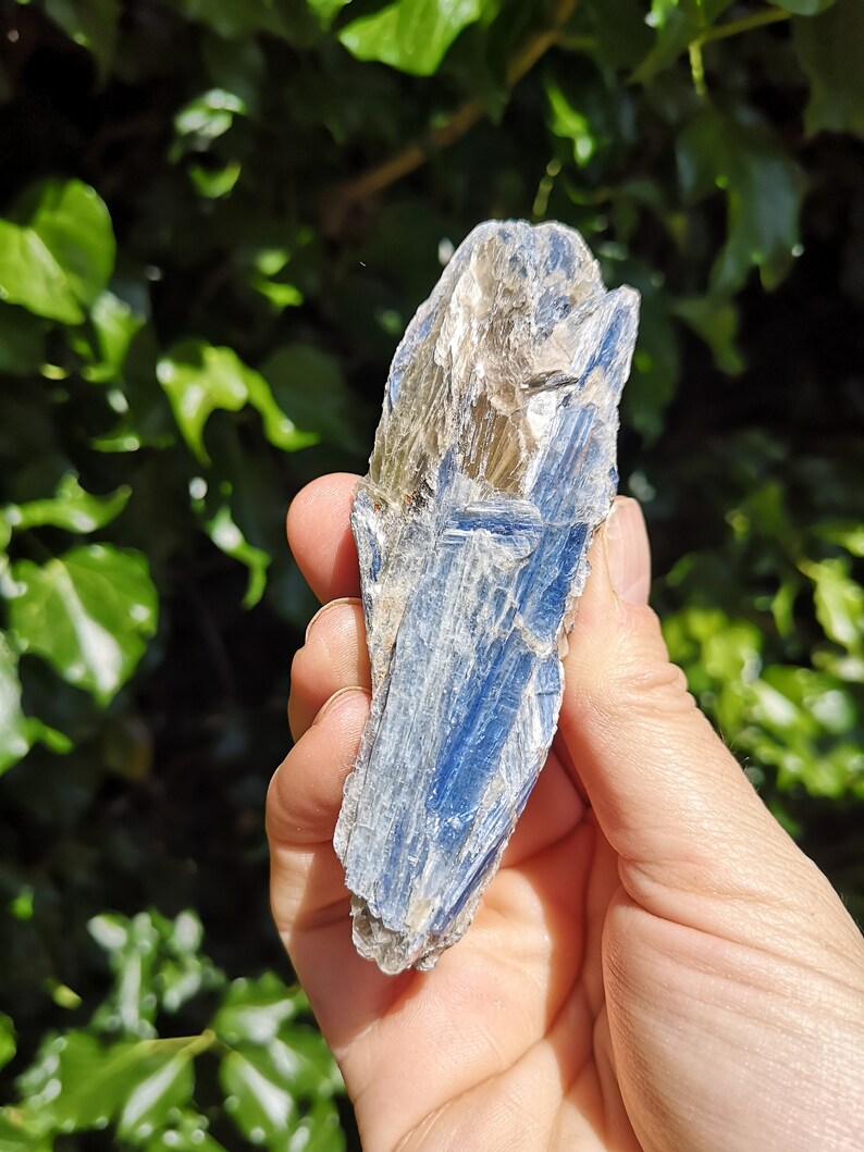 K&ouml;nnte beinhalten: Ein blauer Kyanit-Kristall mit silbernem Schimmer. Der Kristall ist rau und hat ein nat&uuml;rliches, rohes Aussehen.