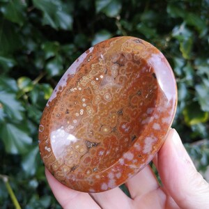 May include: A polished, oval-shaped, brown and white agate bowl with a smooth, polished surface. The bowl has a unique, swirling pattern of brown, white, and orange colors.