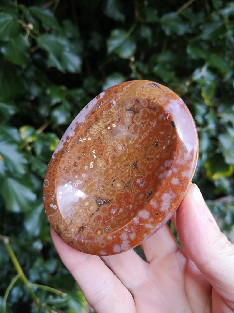 May include: A polished, oval-shaped, brown and white agate bowl with a smooth, polished surface. The bowl has a unique, swirling pattern of brown, white, and orange colors.