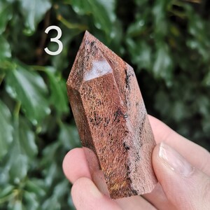 Puede incluir: Una punta de cristal marr&oacute;n y blanca con un patr&oacute;n estriado &uacute;nico. El cristal mide aproximadamente 5 cm de alto y se sostiene en una mano.