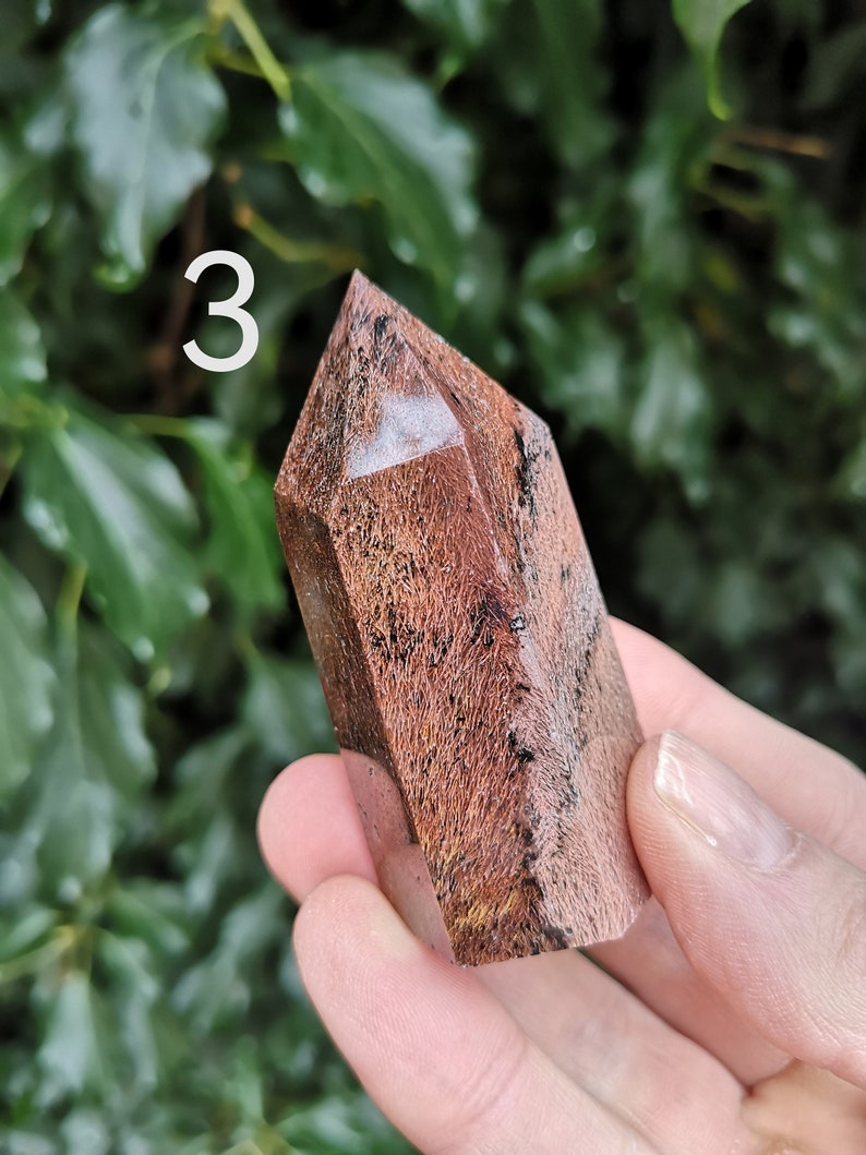 Puede incluir: Una punta de cristal marr&oacute;n y blanca con un patr&oacute;n estriado &uacute;nico. El cristal mide aproximadamente 5 cm de alto y se sostiene en una mano.