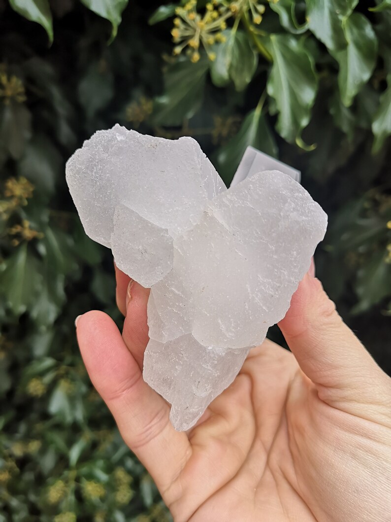 May include: A large, white, translucent crystal cluster with a rough, textured surface. The crystal is shaped like a mountain and has many facets.