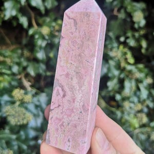 May include: A pink and white striped crystal point, also known as a wand or obelisk. The crystal is smooth and polished.