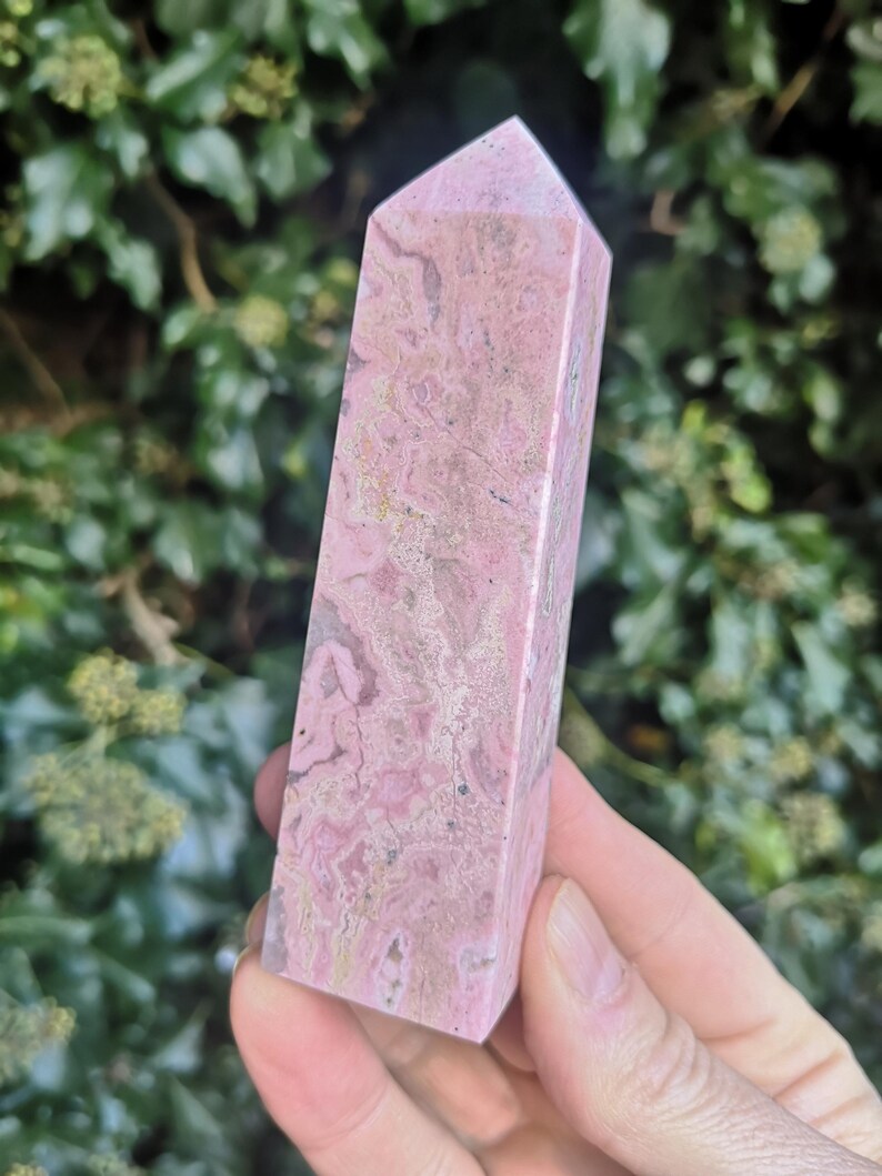 May include: A pink and white striped crystal point, also known as a wand or obelisk. The crystal is smooth and polished.