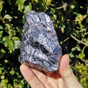May include: A large, metallic grey, irregularly shaped piece of silicon crystal. The crystal has a reflective surface and a rough, textured appearance.