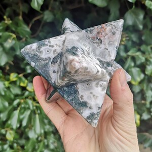 May include: A green, white, and pink agate star shaped crystal. The crystal is carved into a six-pointed star shape.