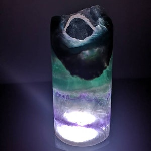 May include: A green, purple, and black fluorite crystal lamp with a white light shining through the center.