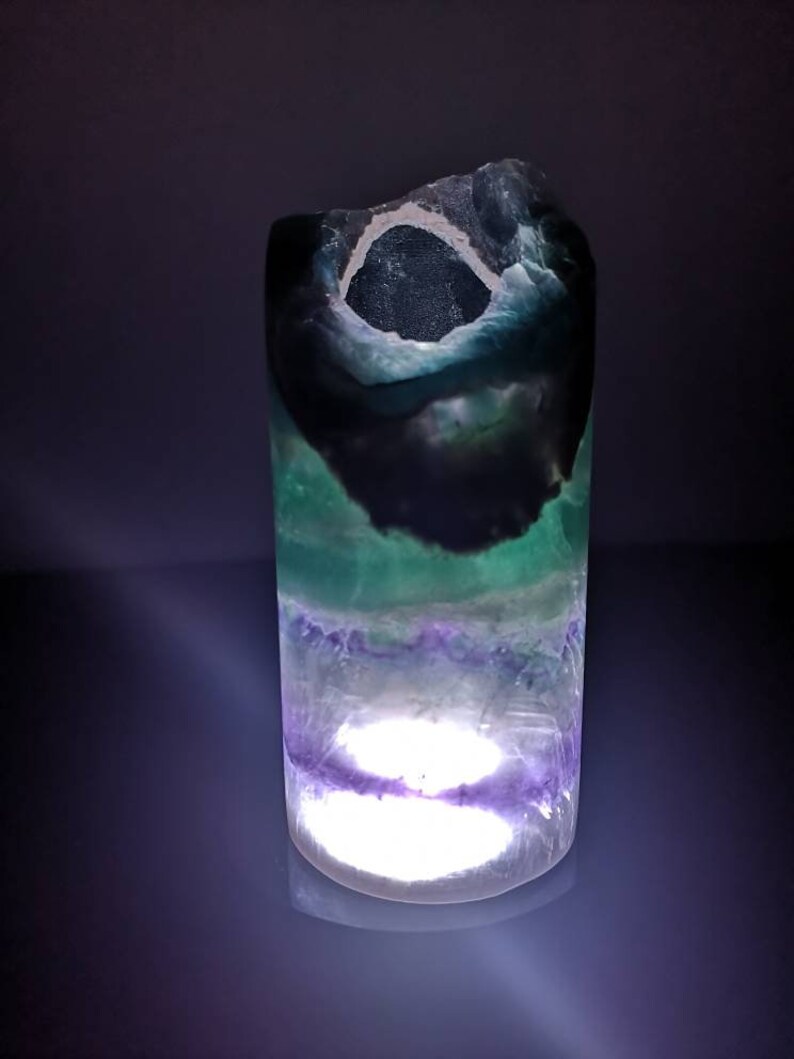 May include: A green, purple, and black fluorite crystal lamp with a white light shining through the center.