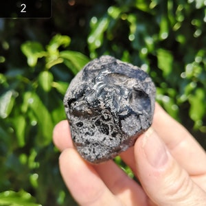 May include: A black obsidian stone with a rough, textured surface. The stone is about the size of a golf ball.