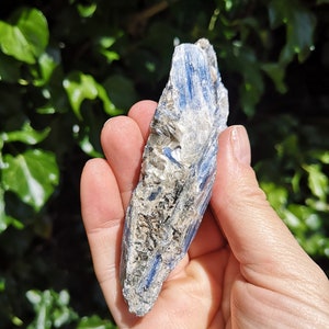 K&ouml;nnte beinhalten: Ein blauer Kyanit-Kristall mit rauer, nat&uuml;rlicher Textur. Der Kristall ist hellblau mit wei&szlig;en und grauen Streifen. Es ist ein roher, unpolierter Kristall.