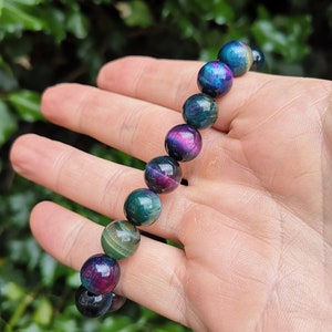 May include: A bracelet made of iridescent tiger's eye beads. The beads are round and have a mix of green, blue, and purple colors.