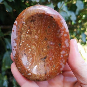 May include: A polished, oval-shaped, red and white agate dish with a unique, swirling pattern. The dish is made of natural stone and has a smooth, polished surface.