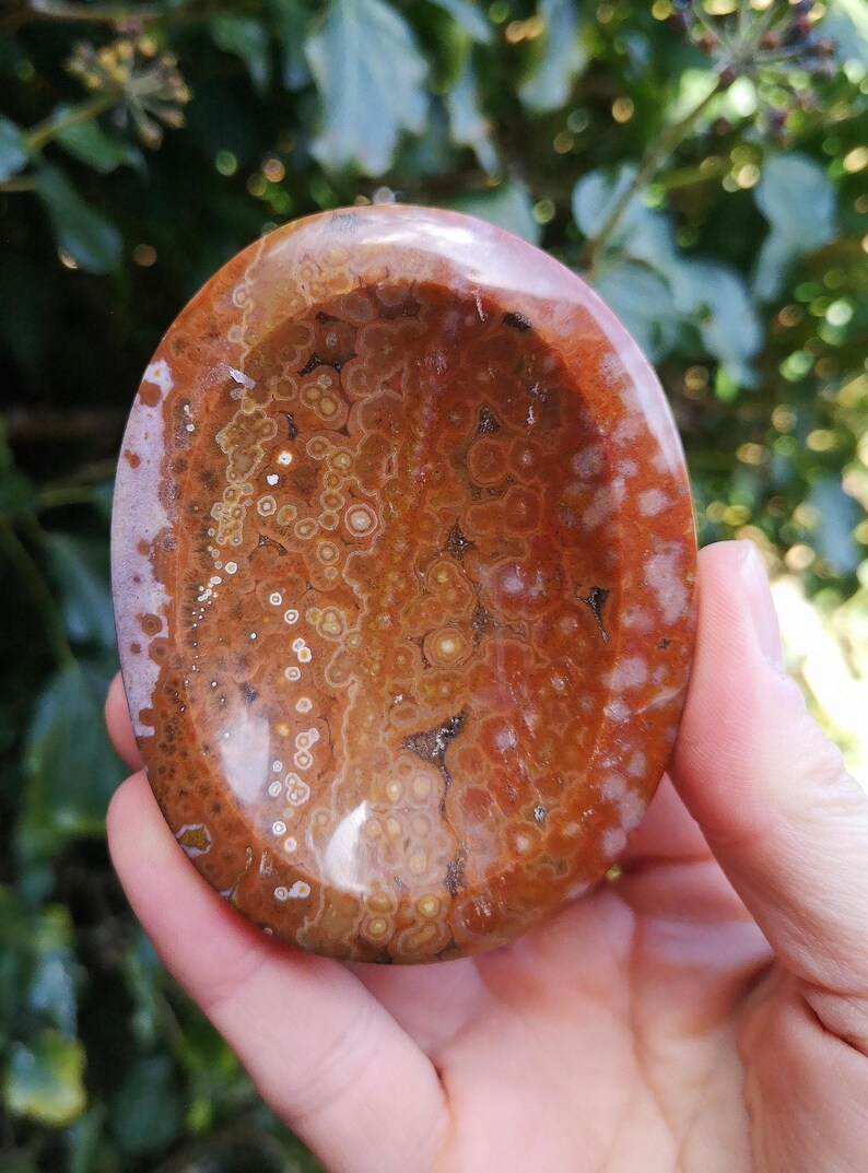 May include: A polished, oval-shaped, red and white agate dish with a unique, swirling pattern. The dish is made of natural stone and has a smooth, polished surface.