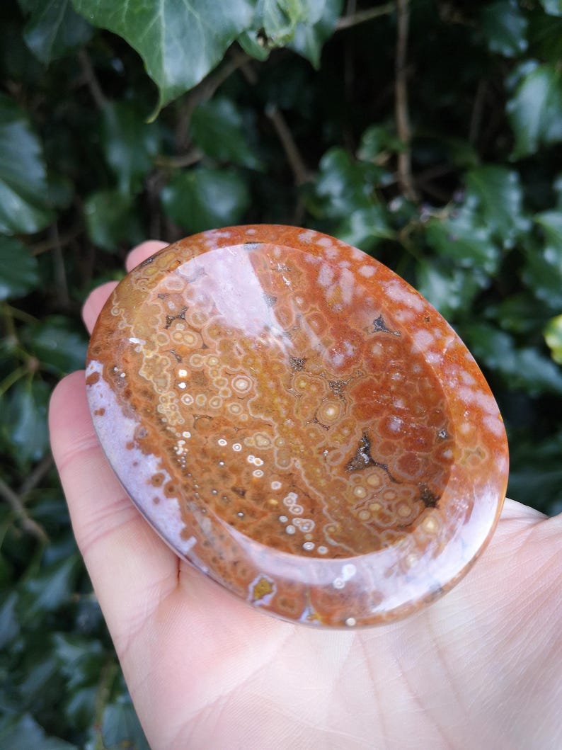 May include: A polished oval-shaped dish made from brown and white agate with a swirling pattern. The dish is perfect for holding small items like jewelry or crystals.