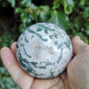 May include: A green and white agate sphere with a swirling pattern. The sphere is smooth and polished.