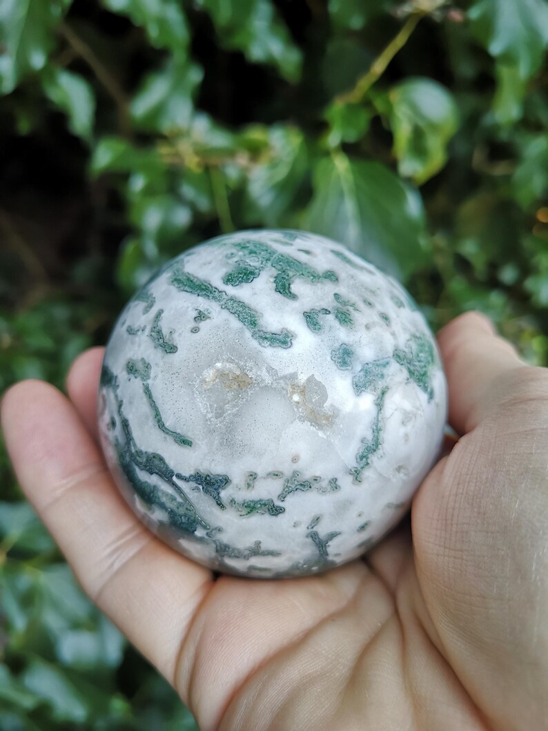 May include: A green and white agate sphere with a swirling pattern. The sphere is smooth and polished.