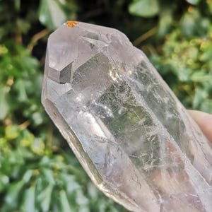 May include: A large, clear quartz crystal with a double termination. The crystal has a natural, raw appearance with visible inclusions and striations.