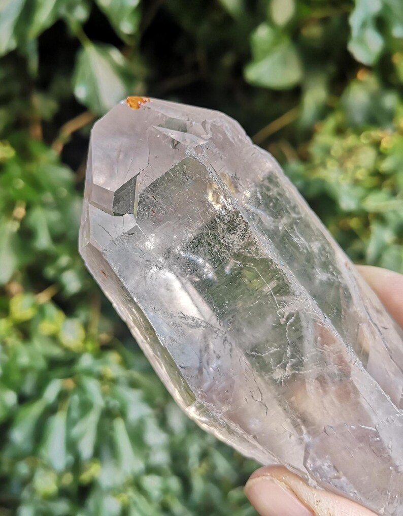 May include: A large, clear quartz crystal with a double termination. The crystal has a natural, raw appearance with visible inclusions and striations.