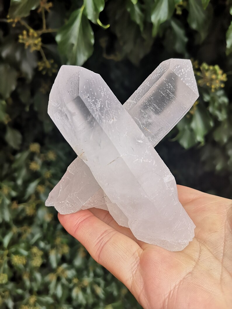 May include: A cluster of clear quartz crystals with a pointed shape, arranged in a cross formation. The crystals are translucent and have a natural, rough texture.