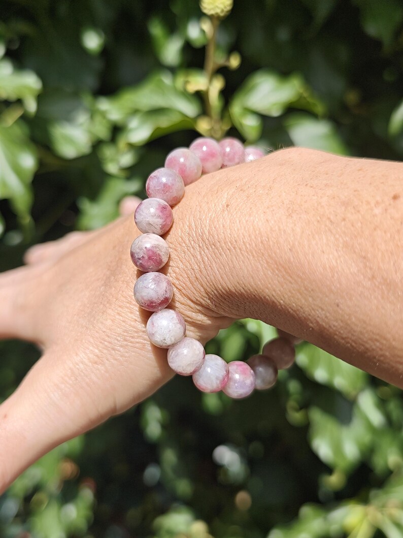 May include: A stretch bracelet composed of round, polished beads in varying shades of pink, white, and translucent rose. The beads feature natural marbling and internal inclusions, creating a unique pattern on each stone within the circular design.