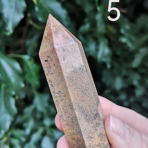Puede incluir: Una punta de cristal marr&oacute;n y negro con una punta puntiaguda. El cristal tiene una textura natural y rugosa.