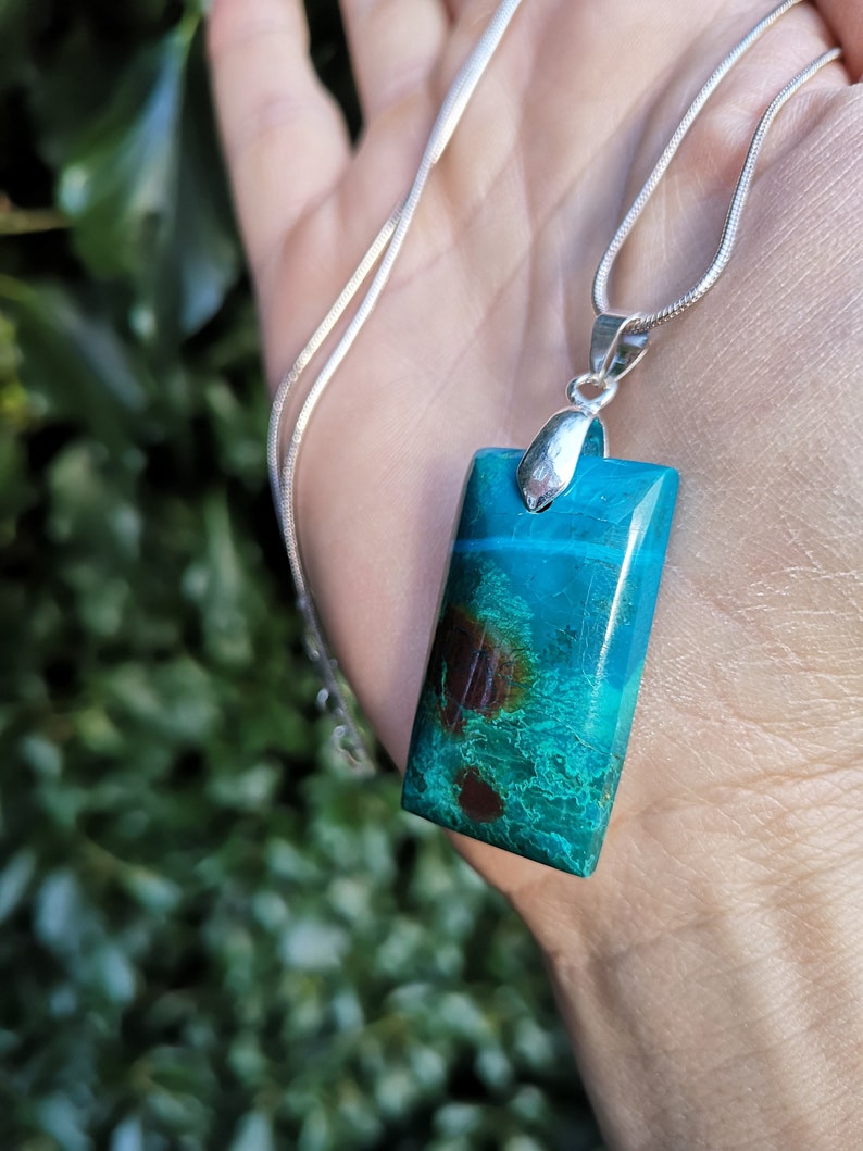 Pu&ograve; includere: Collana con pendente rettangolare turchese con inclusioni marroni e verdi. La catena &egrave; argentata. Il pendente &egrave; rettangolare e ha un'attaccatura argentata.