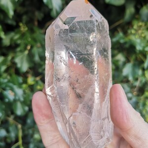 May include: A large, clear quartz crystal with a pointed tip and a natural, rough texture. The crystal is translucent and has a slight pink hue.