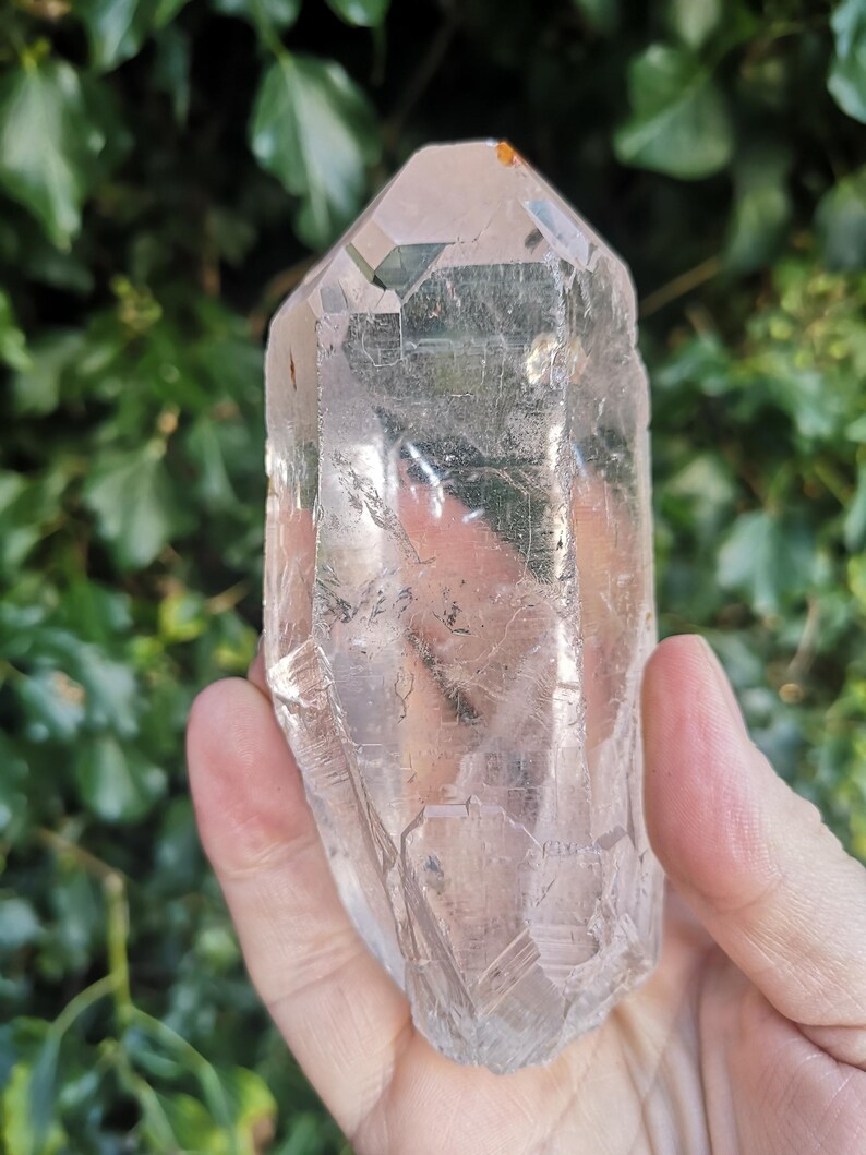 May include: A large, clear quartz crystal with a pointed tip and a natural, rough texture. The crystal is translucent and has a slight pink hue.