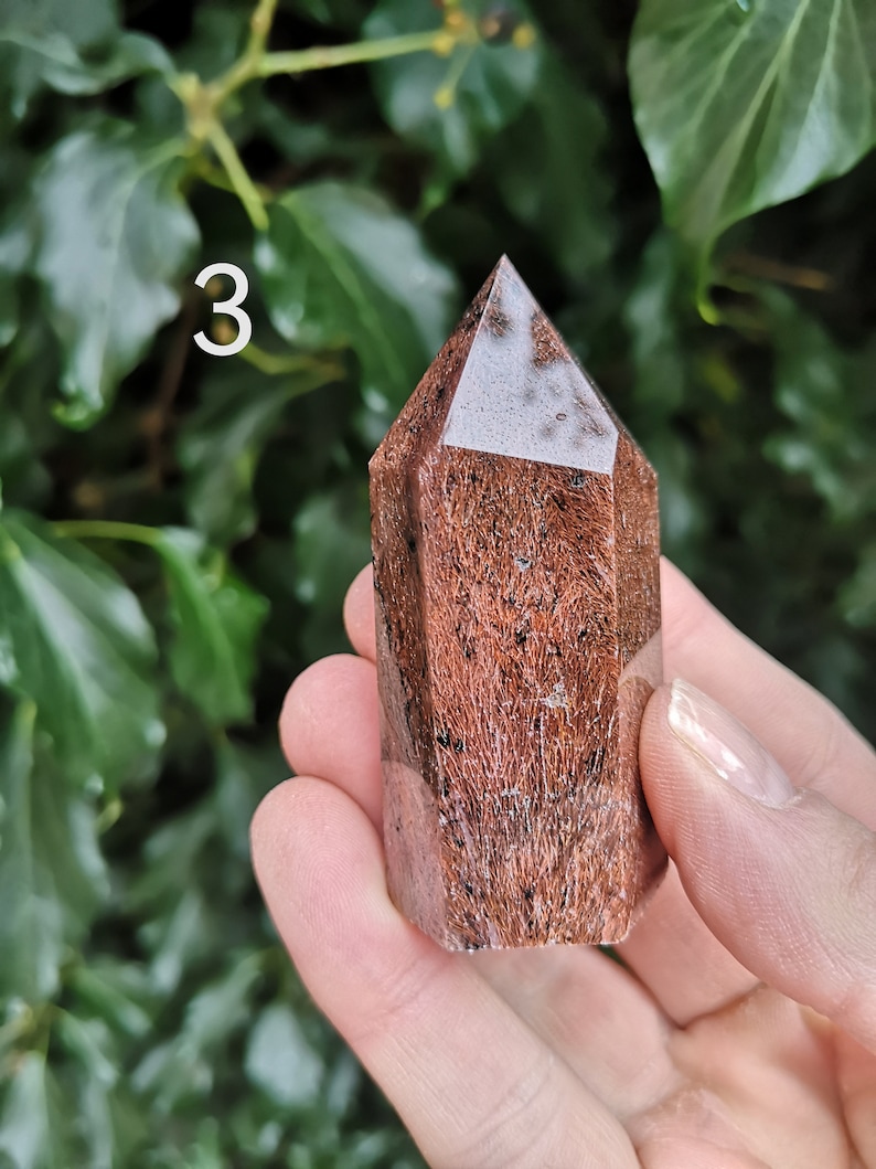 Puede incluir: Una punta de cristal marr&oacute;n y blanco con una parte superior puntiaguda y una base facetada. El cristal mide aproximadamente 5 cm de alto y tiene una textura natural y rugosa.