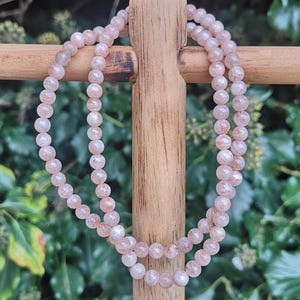 May include: A double strand necklace made of small, round, light pink sunstone beads. The beads have a shimmery, iridescent quality.