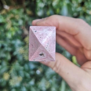 May include: A pink and white pyramid-shaped crystal with black flecks.