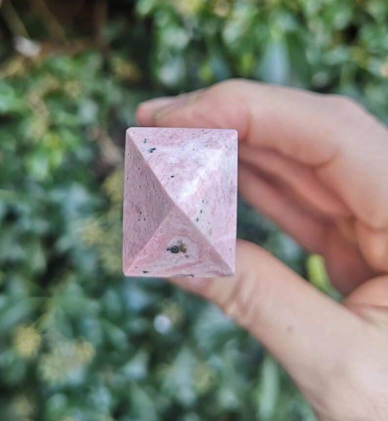 May include: A pink and white pyramid-shaped crystal with black flecks.