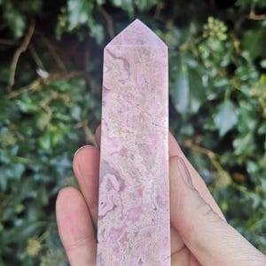May include: A pink and white crystal point with a pointed top and a smooth, polished surface. The crystal has a marbled pattern with swirls of pink and white.