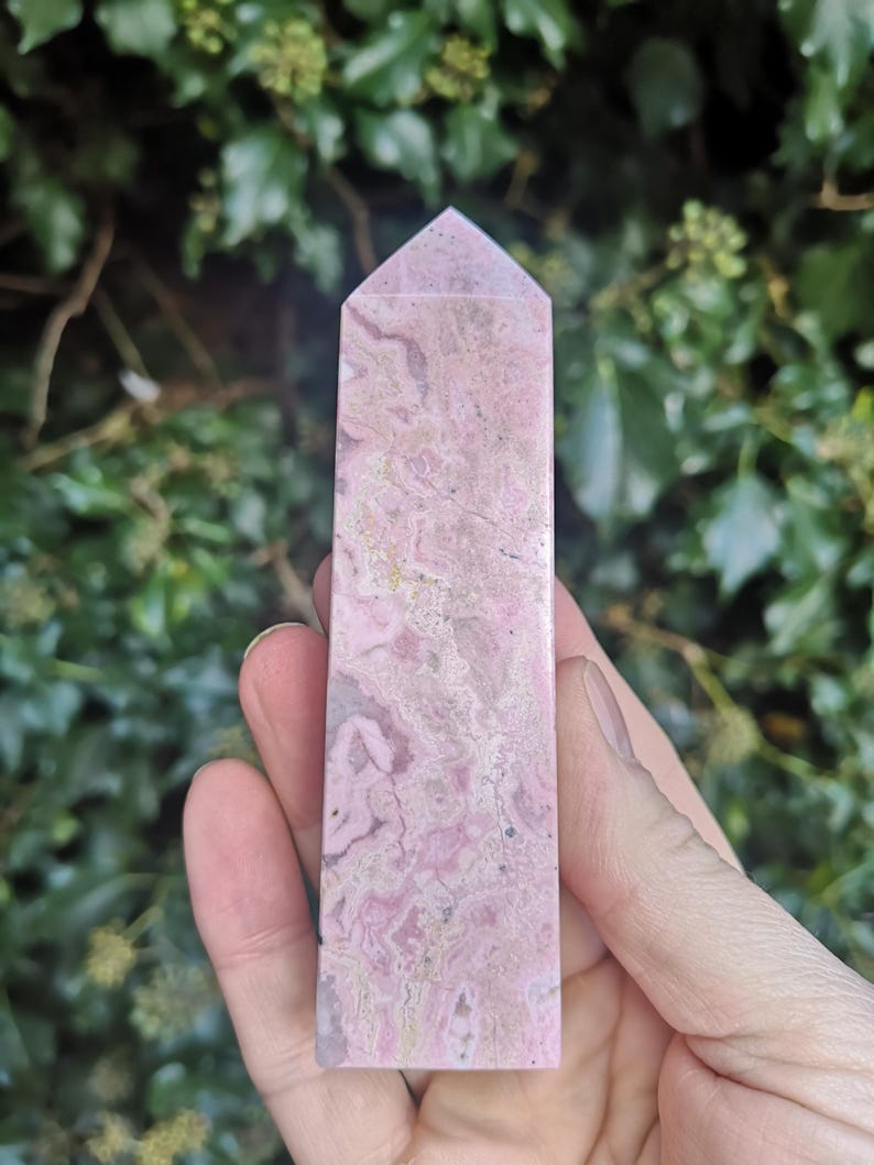 May include: A pink and white crystal point with a pointed top and a smooth, polished surface. The crystal has a marbled pattern with swirls of pink and white.