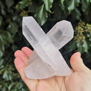 May include: A cluster of clear quartz crystals, with a pointed shape, arranged in a cross formation. The crystals are translucent and have a smooth, polished surface.
