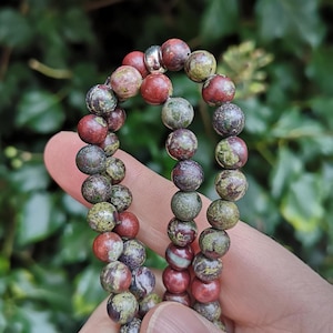 May include: A beaded bracelet made of red, green, and brown jasper stones. The bracelet has a silver spacer bead.