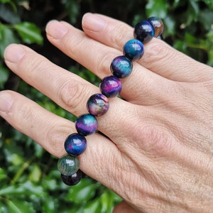 May include: A bracelet made of iridescent tiger's eye beads in shades of blue, green, and purple. The beads are round and have a smooth, polished finish.