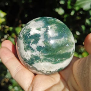 May include: A green and white agate sphere, polished to a smooth finish. The sphere has a swirling pattern of green and white, resembling clouds.