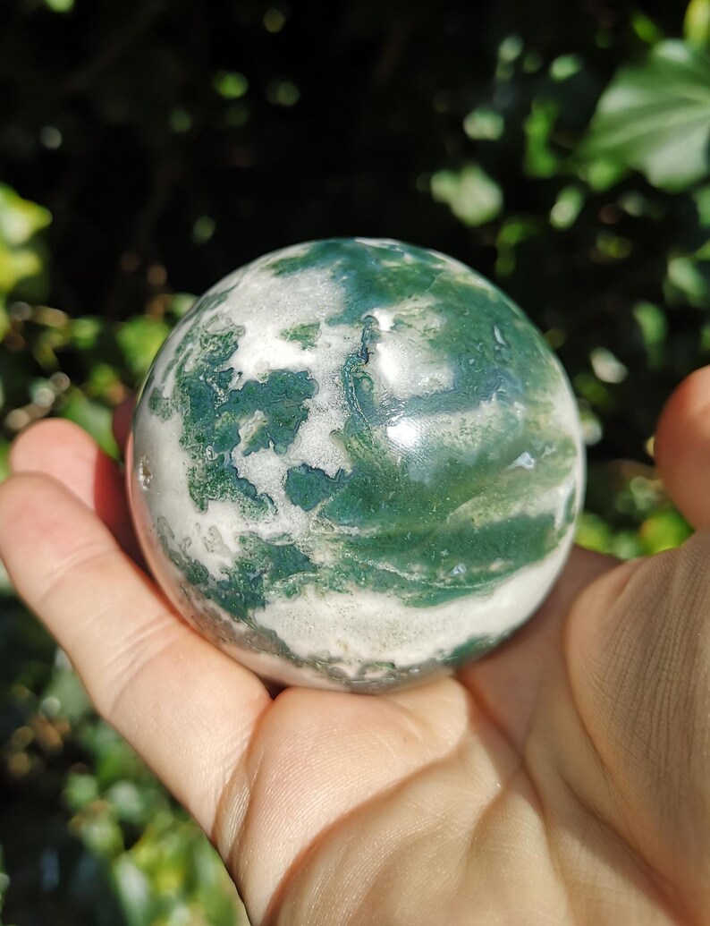 May include: A green and white agate sphere, polished to a smooth finish. The sphere has a swirling pattern of green and white, resembling clouds.