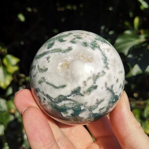 May include: A green and white agate sphere with a swirling pattern. The sphere is smooth and polished.