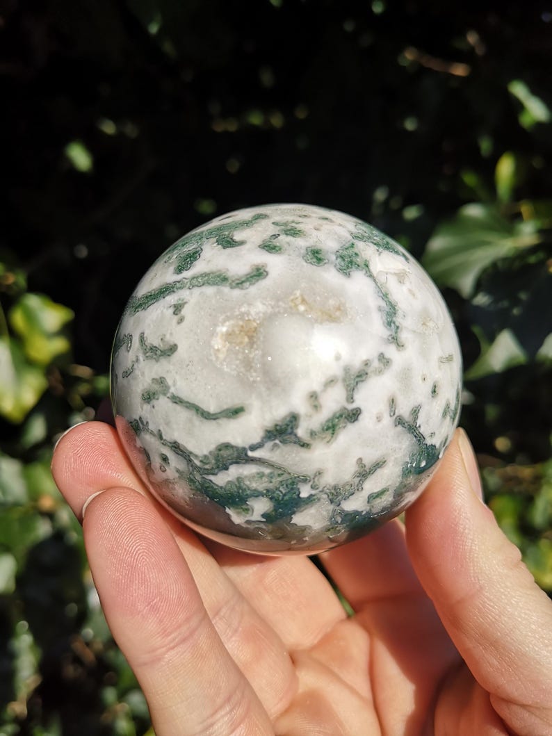 May include: A green and white agate sphere with a swirling pattern. The sphere is smooth and polished.