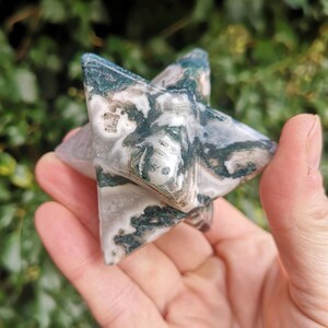 May include: A six-pointed star carved from green and white moss agate. The star is smooth and polished, with a natural, organic look.