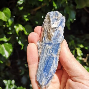 K&ouml;nnte beinhalten: Ein blauer Kyanit-Kristall mit silbernem Schimmer. Der Kristall ist an einem Ende spitz und hat eine raue, nat&uuml;rliche Textur.