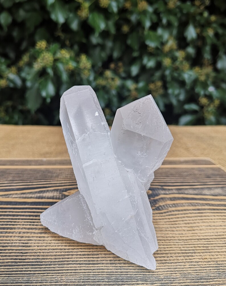 May include: A cluster of clear quartz crystals with a rough, natural texture. The crystals are arranged in a triangular shape, with the largest crystal in the centre.