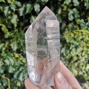 May include: A large, clear quartz crystal point with a pointed tip and a flat base. The crystal is translucent and has a slight shimmer.