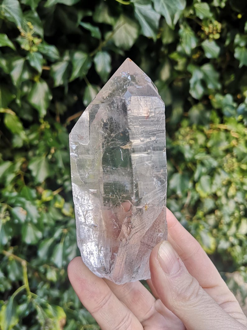 May include: A large, clear quartz crystal point with a pointed tip and a flat base. The crystal is translucent and has a slight shimmer.