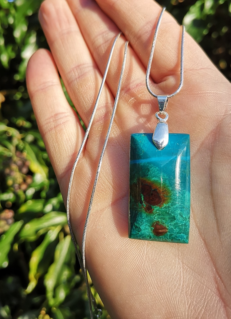 Pu&ograve; includere: Una collana con pendente rettangolare con una pietra turchese e marrone. La pietra &egrave; incastonata in metallo color argento e pende da una delicata catena d'argento. Il pendente ha una finitura lucida e brillante.