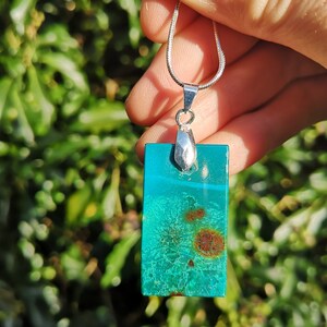 Pu&ograve; includere: Collana con pendente rettangolare e catena d'argento. Il pendente &egrave; una vibrante pietra turchese con inclusioni marroni e ruggine. Il pendente &egrave; lungo circa 3,8 cm.