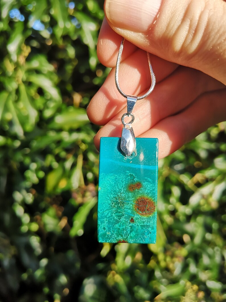 Pu&ograve; includere: Collana con pendente rettangolare e catena d'argento. Il pendente &egrave; una vibrante pietra turchese con inclusioni marroni e ruggine. Il pendente &egrave; lungo circa 3,8 cm.
